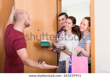 Smiling guests with cake and presents standing in doorway