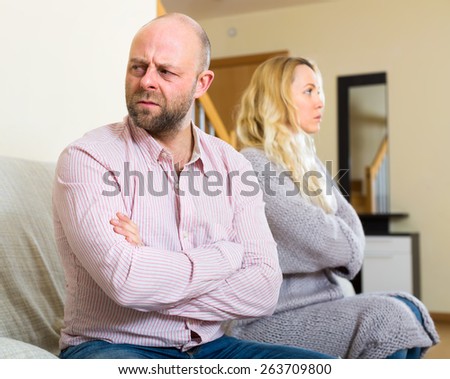 Sad husband sitting on a couch turned away from his wife after they had a quarrel