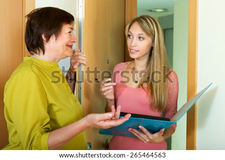 Elderly woman answers the questions of young employee  in door at home