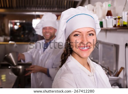 Cheerful smiling cooks working at kitchen in take-away restaurant