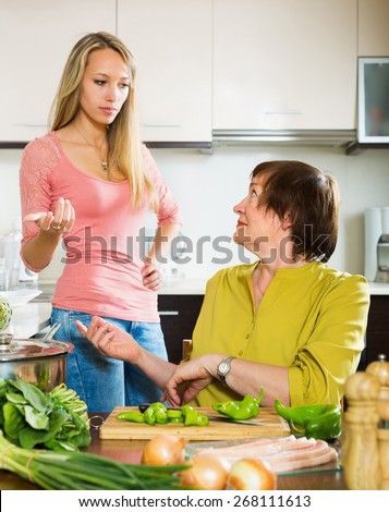 Mature female with sad adult daughter sharing bad news in kitchen