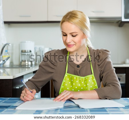 Smiling woman at kitchen signing contractual agreement for renting new flat