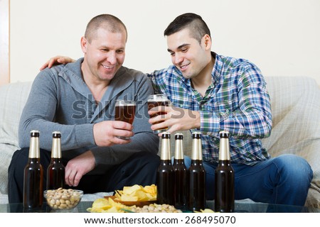 Young man drinks beer with old friend at home