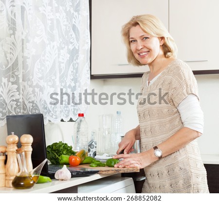 Smiling mature woman  with notebook  cooking soup  in home\'s kitchen