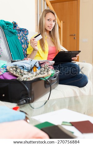 Pretty girl with packed suitcase booking hotel online with credit card