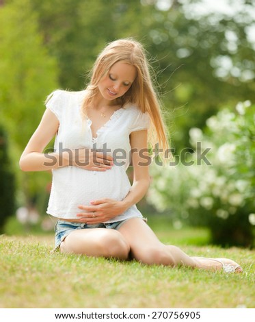 Long-haired funny pregnant woman on the grass in the summer park