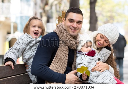 Young parents with their children sitting outside on a bench and having fun. Shallow focus. Focused on a man.