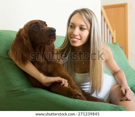 Long-haired girl sitting on sofa at home with red Irish setter