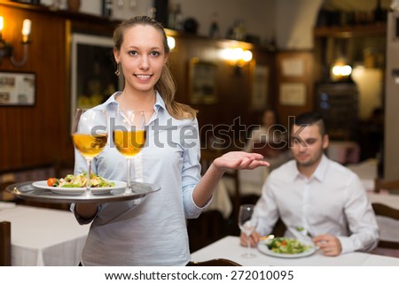 Positive waitress holding tray with glasses of wine in bar