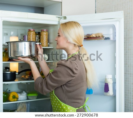 Blonde girl looking for something in fridge at home kitchen