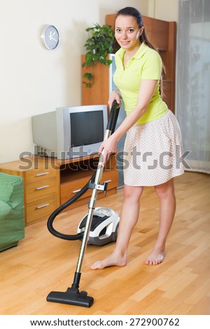 Cheerful young woman in skirt cleaning with vacuum cleaner at home