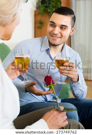 Young guy and elderly blonde woman drinking wine and smiling indoor