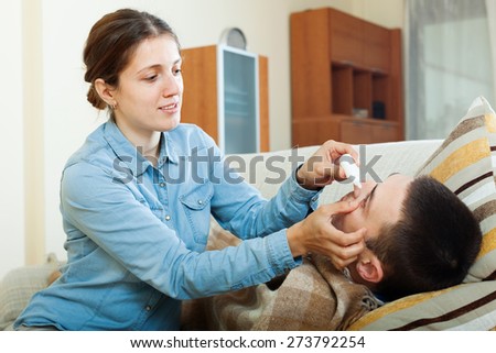 Caring woman dripping eye drops to man in home