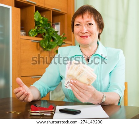 Smiling elderly woman sitting with money and documents at the table