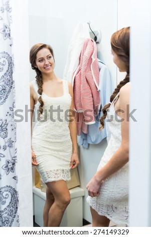 Beautiful smiling girl standing in front of mirror at boutique changing cubicle