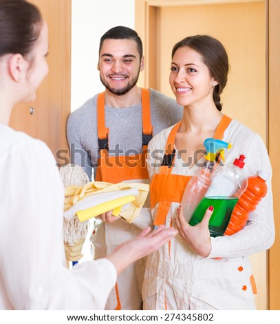 Housewife meeting cleaning crew with equipment at doorway. Focus on girl