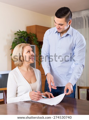Son helping smiling senior mother with documents for buying apartment