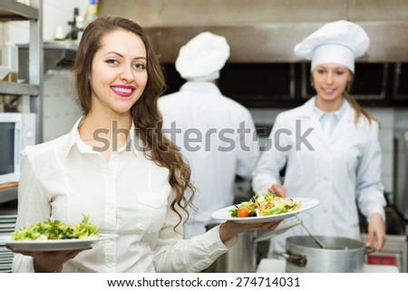 Team of positive chefs and young waiter in restaurant kitchen