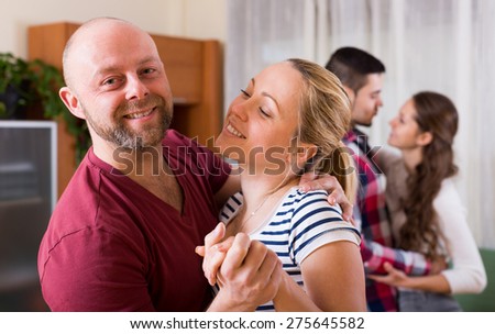 Two couples smiling and moving in slow dance indoors