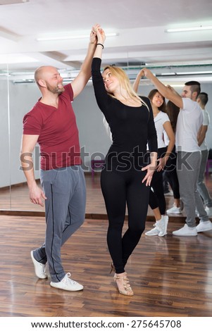 Smiling adult couples enjoying of partner dance indoor