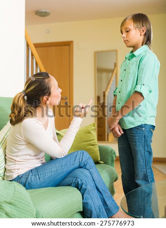 Serious mother scolding teenage son in home interior. Focus on woman