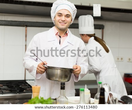 Two professional cooks working at restaurant kitchen together. Focus on man