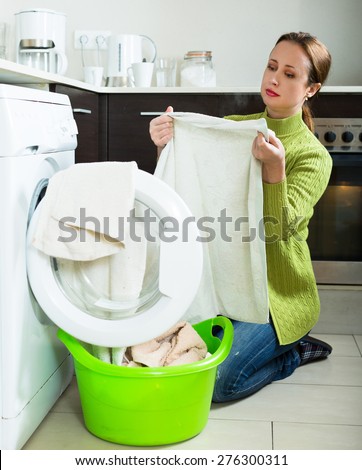tired woman in green doing laundry with washing machine at home kitchen