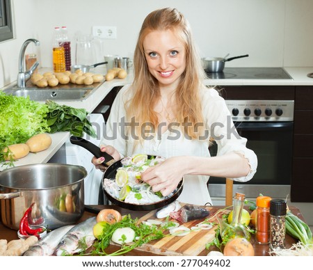 Smiling girl cooking fish in meal in frying pan at home kitchen