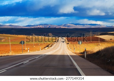 Landscape with road among fields and hills under  cloudy sky