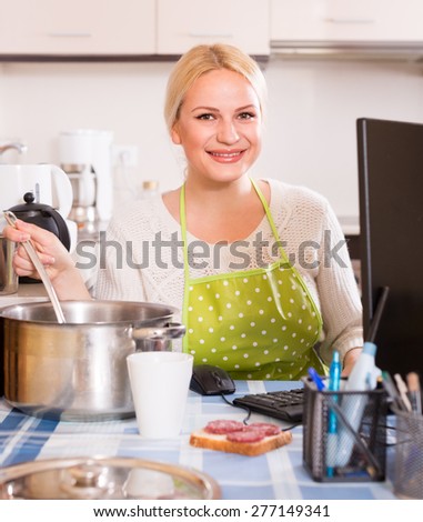 freelancer 25-30 years old with dishware working on PC at kitchen