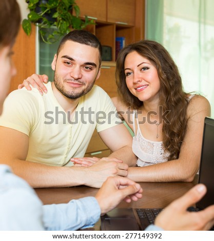 Young married couple talking with employee with laptop and smiling
