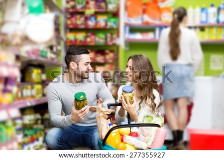 Young smiling couple standing near shelves with canned goods at shop