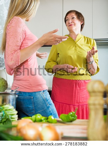 Elderly mother and adult daughter having serious conversation at kitchen