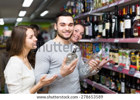 Cheerful shoppers with bottles of vodka at supermarket. Focus on guy