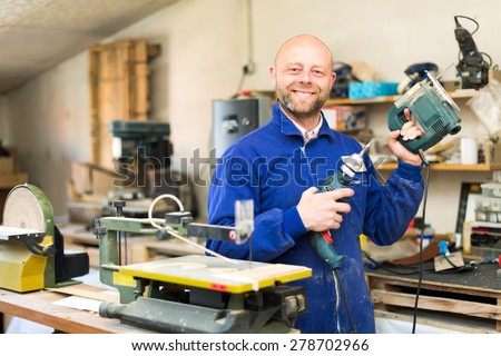 Happy woodworker posing with instruments for wood processing in a workshop indoors