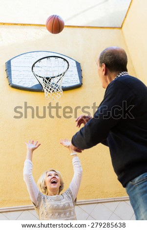 Cheerful smiling couple of pensioners playing basketball in patio