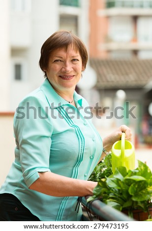 Portrait of elderly woman watering domestic plants on terrace