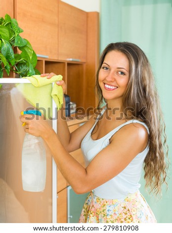 Happy smiling young housewife cleaning glass door of furniture at home