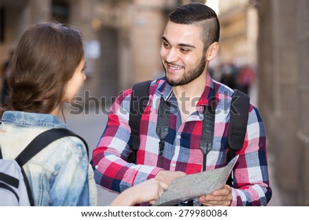 Positive young man and woman with luggage walking through city street