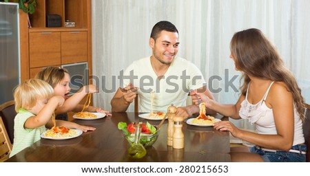 Young family of four having lunch with spaghetti at home. Focus on man