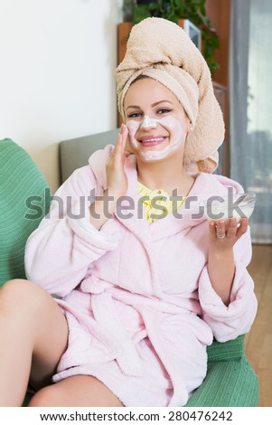 Happy young girl lying on couch with cream over face indoors