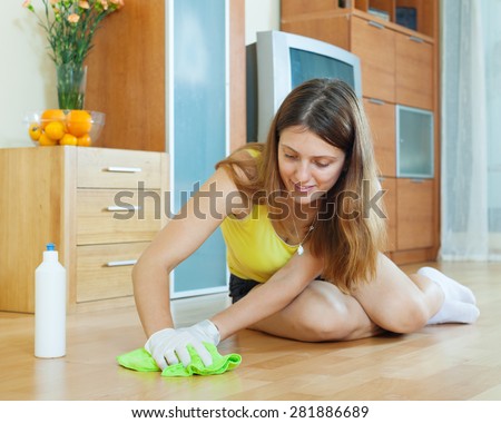 young woman rubbing wooden floor with rag and cleanser at home