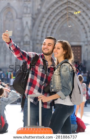 Tourist couple with luggage doing selfie at travel destination background