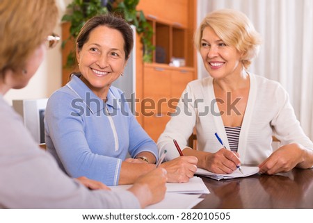Positive senior women signing documents at notary. Focus on brunette