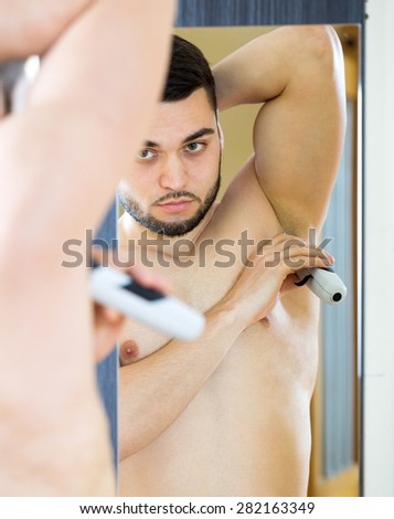 Young guy shaving armpit with electric razor