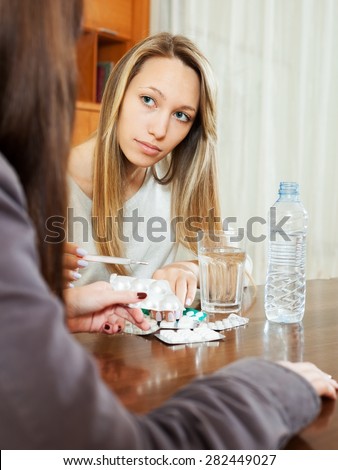 Sick woman looking by thermometer at home, friend helping her