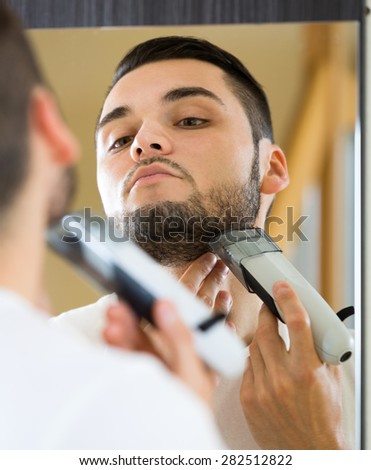 Man looking at mirror and shaving face with electric razor