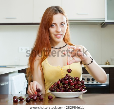 Positive young woman with cherry in domestic kitchen