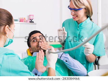 Blonde female dentist with assistant and scared male patient at dental clinic