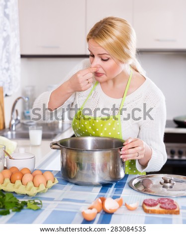 Young female takes lid off pan and feel musty smell at home kitchen